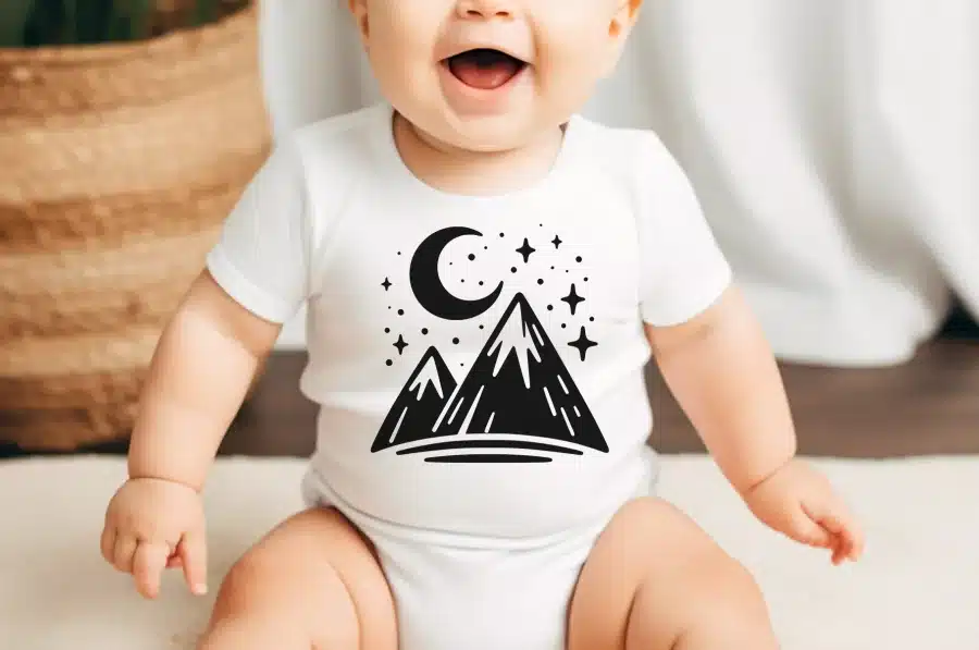Baby Wearing A White Bodysuit With A Black Mountain Range And Crescent Moon Design.