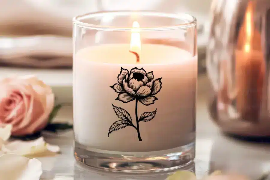 A lit candle in a glass jar decorated with a black and white floral design.