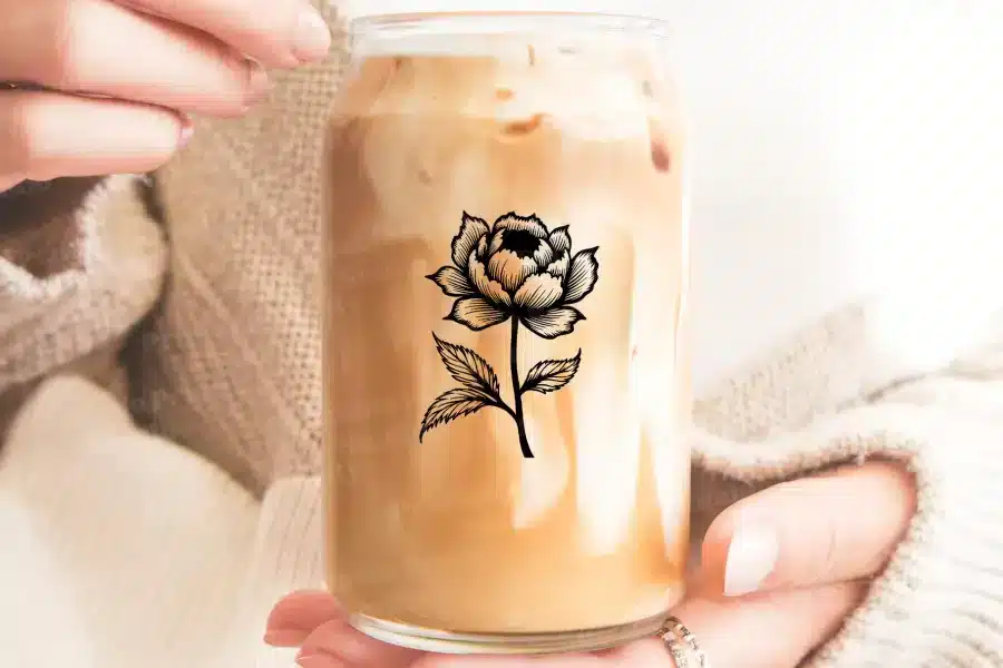 A Person'S Hands Holding A Glass Iced Coffee With A Black Peony Graphic.