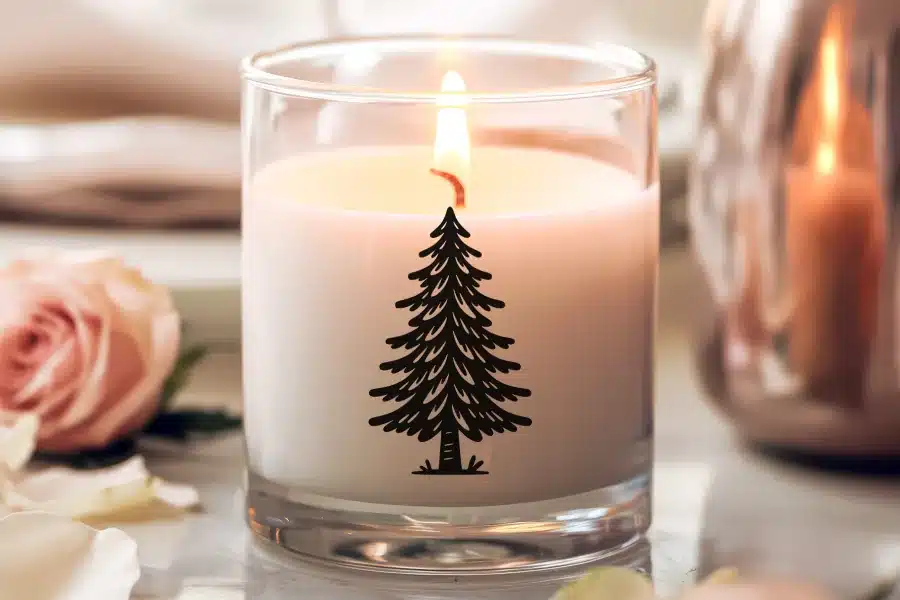 Lit candle in a glass jar with a black evergreen tree design.