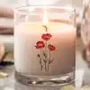 A Lit Candle In A Clear Glass Jar, Decorated With A Simple Design Of Three Red Poppies.