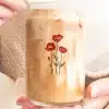 A Person'S Hands Holding A Glass Iced Coffee Can With A Floral Design.