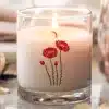 A Lit Candle In A Clear Glass Jar With A Poppy Flower Design.