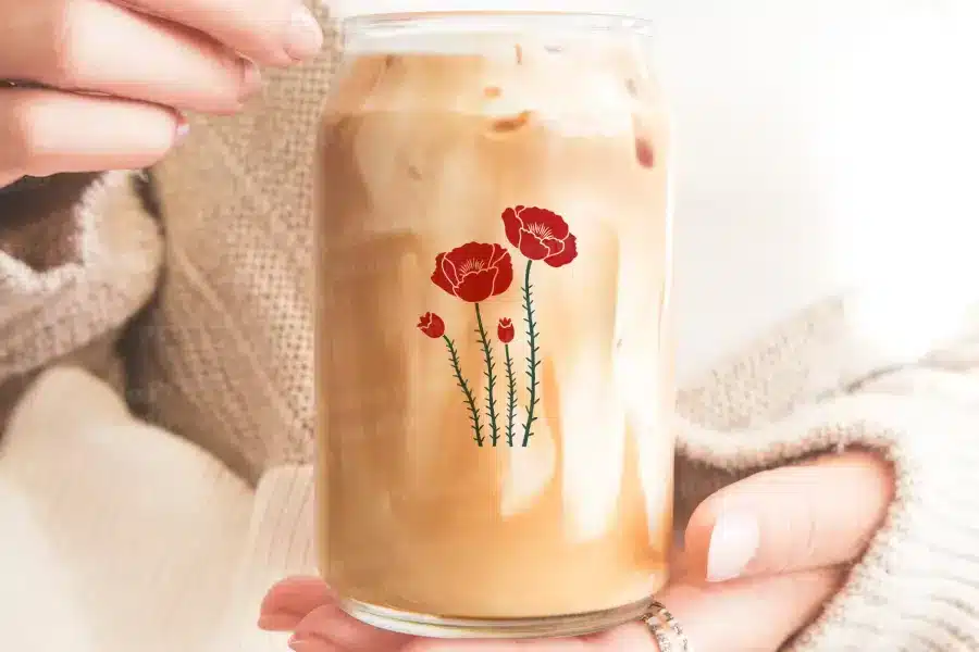 Hands Holding A Glass Iced Coffee With A Poppy Flower Design.