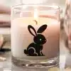 A Lit Candle In A Glass Jar Features A Black Bunny Rabbit Design.