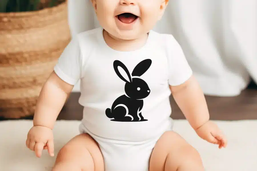 Baby wearing a white bodysuit with a black rabbit design.