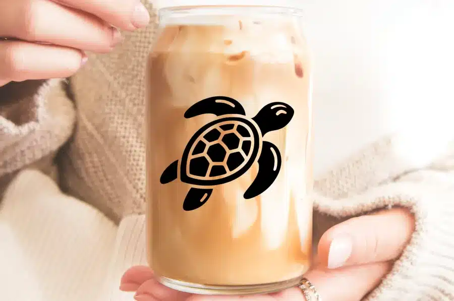 Close-Up Of Hands Holding A Glass Iced Coffee With A Sea Turtle Decal.