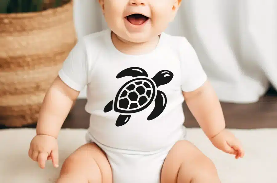 Baby Wearing A White Bodysuit With A Black Sea Turtle Graphic.