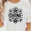 Woman Wearing A White T-Shirt With A Shine Bright Design Featuring Stars.