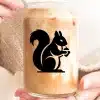 A Person'S Hands Holding An Iced Coffee In A Glass Jar With A Black Silhouette Of A Squirrel Holding An Acorn.