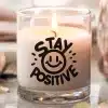 A Lit Candle In A Glass Jar With A Smiley Face And The Words Stay Positive.