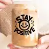 A Person Holds A Glass Iced Coffee With The Words Stay Positive And A Smiley Face Printed On It.