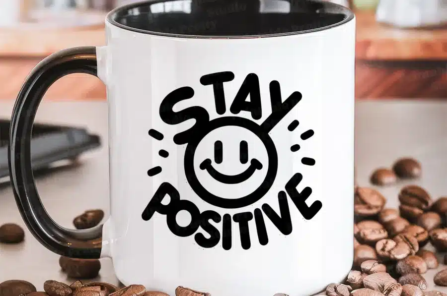 White Coffee Mug With A Black Handle, Featuring A Black Graphic That Says Stay Positive And Includes A Smiling Face.