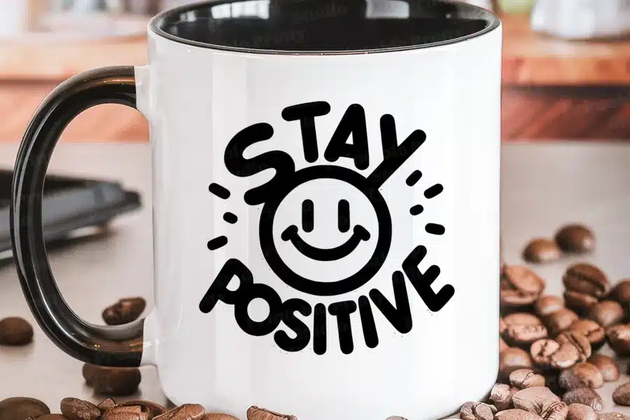 White coffee mug with a black handle, featuring a black graphic that says Stay Positive and includes a smiling face.