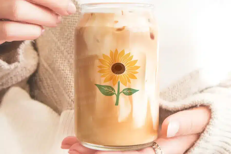 A Person'S Hands Hold A Glass Iced Coffee Can With A Sunflower Design.