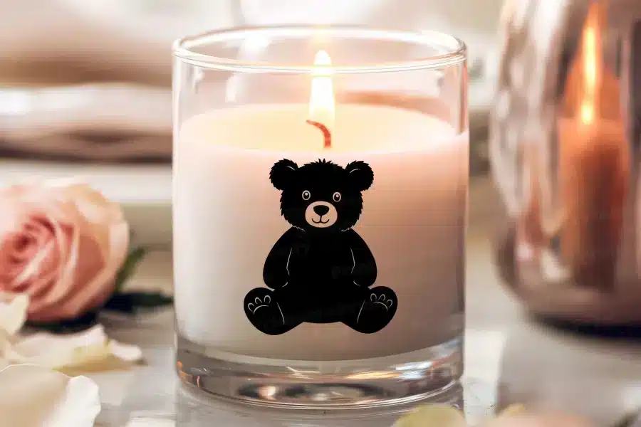A Lit Candle With A Black Teddy Bear Silhouette On Its Side.