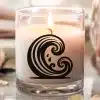 A Lit Candle In A Clear Glass Jar With A Black Wave Design.
