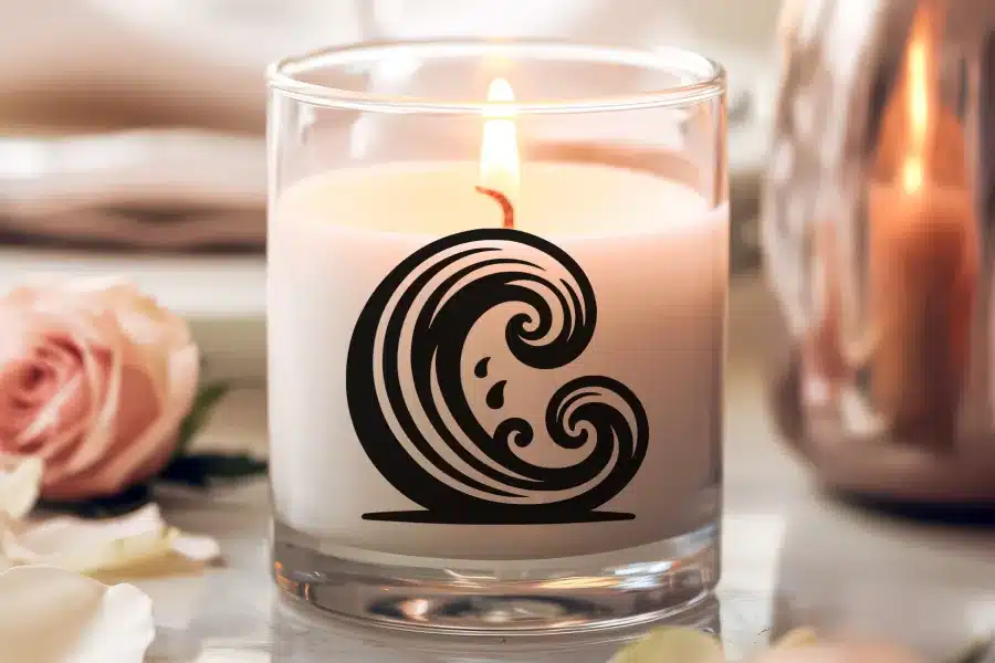 A lit candle in a clear glass jar with a black wave design.