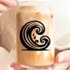 A Person Holds A Glass Jar Filled With Iced Coffee.  A Stylized Wave Design Is On The Jar.