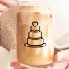 A Person Holds A Glass Jar Filled With Iced Coffee. A Simple Line Drawing Of A Wedding Cake With A Heart On Top Is On The Jar.