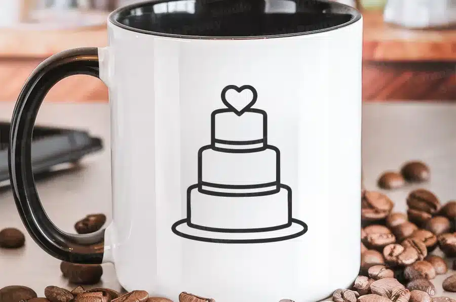 White Coffee Mug With A Black Handle, Featuring A Line Drawing Of A Three-Tiered Wedding Cake Topped With A Heart.