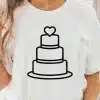 Woman Wearing A White T-Shirt With A Black Line Drawing Of A Three-Tiered Wedding Cake Topped With A Heart.