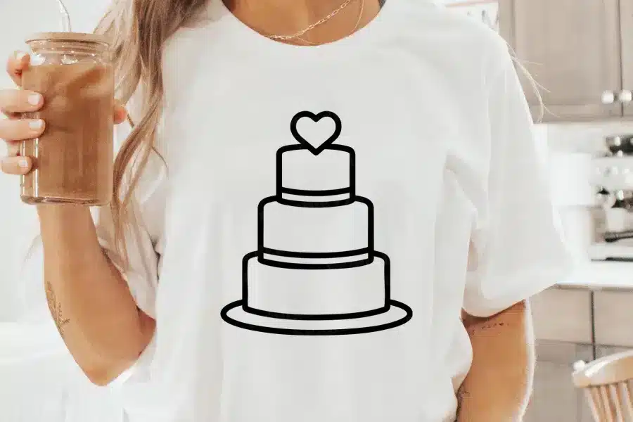 Woman Wearing A White T-Shirt With A Black Line Drawing Of A Three-Tiered Wedding Cake Topped With A Heart.