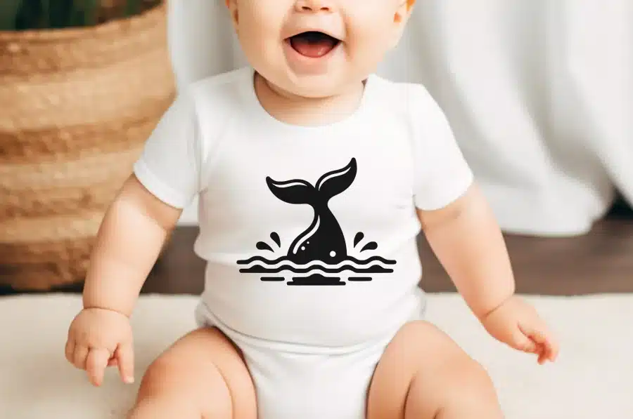 Baby Wearing A White Onesie With A Black Whale Tail Design.