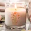 A Lit Candle In A Clear Glass Jar With A Floral Design.