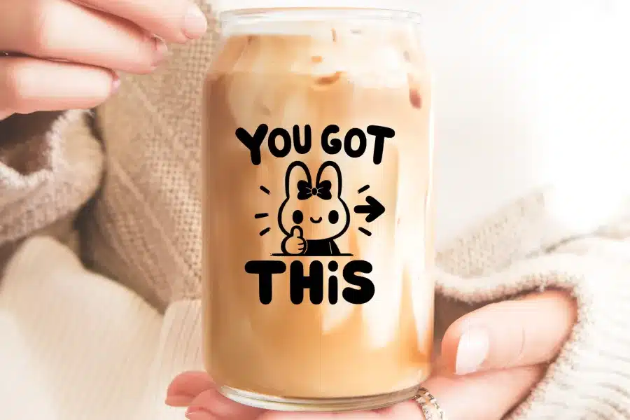 Hands hold a glass iced coffee can with a cute bunny graphic and the text You Got This.
